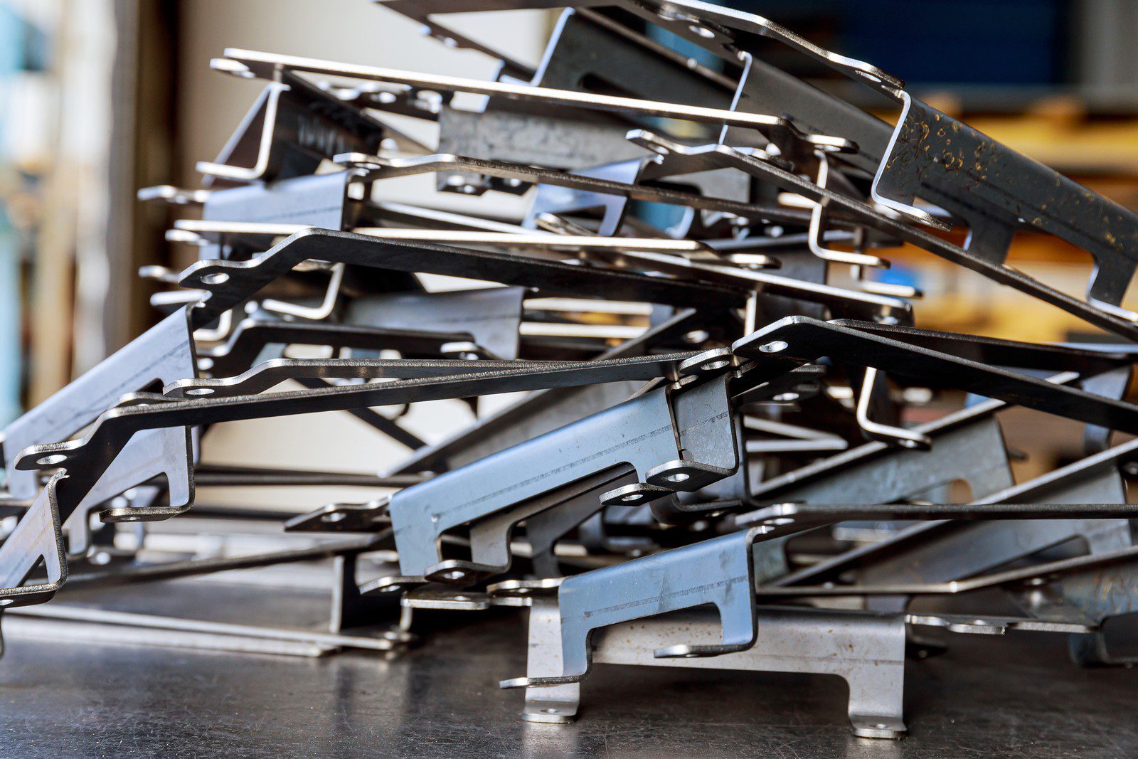 This image shows a stack of metal brackets or parts, likely fabricated for industrial or mechanical use. They have a variety of holes and cuts, suggesting that they are designed to be assembled with other components. The metal appears to have a protective coating, possibly galvanization or paint, to prevent corrosion. The context suggests a manufacturing or workshop environment.